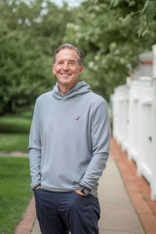 Mark Zides outdoors in a grey hoodie, smiling, hands in pockets.