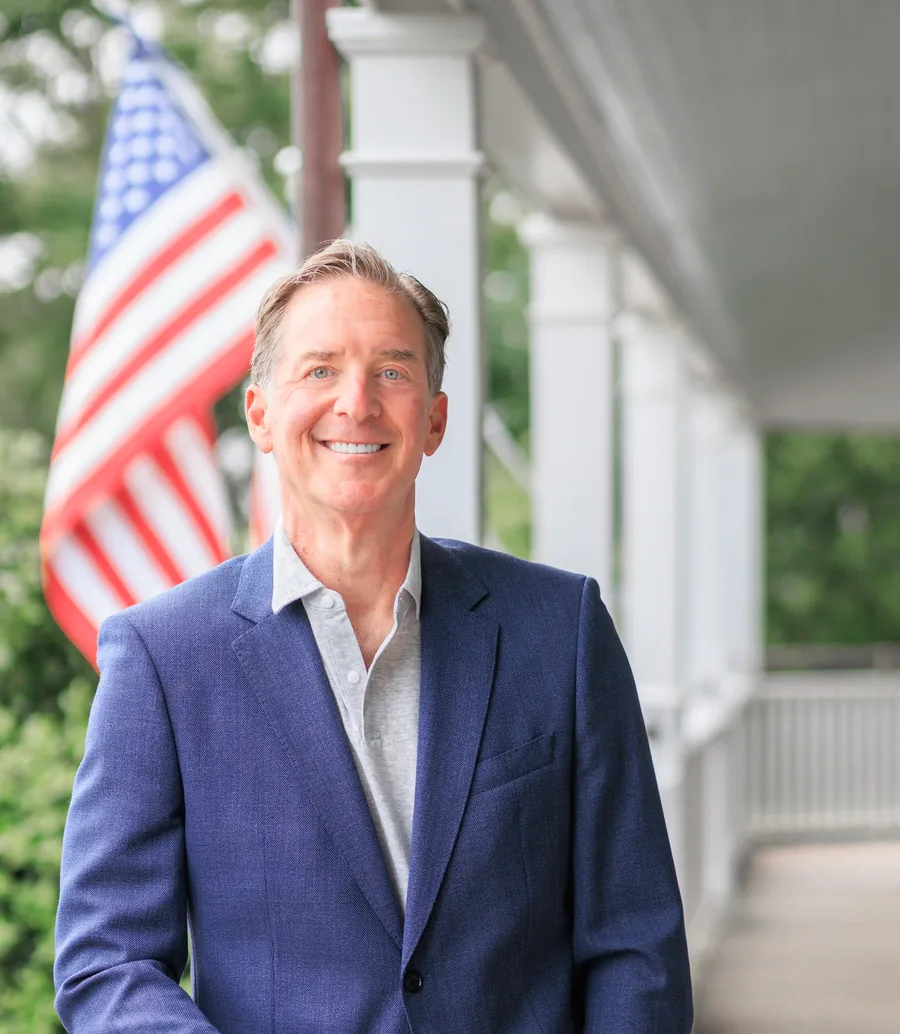 Mark Zides on a porch, smiling, wearing a blue blazer.