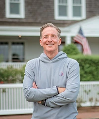 Mark Zides standing outside a shingled house, arms crossed.