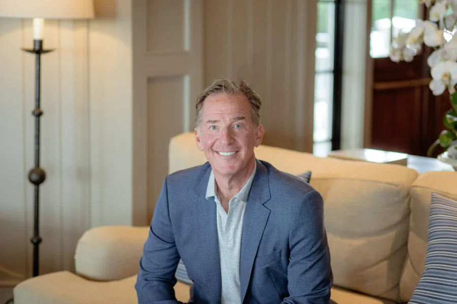 Mark Zides seated indoors on a sofa, in a blue blazer.
