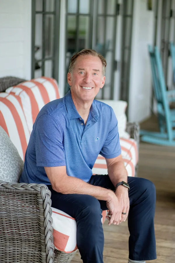 Mark Zides seated in a wicker porch chair in a blue polo shirt.