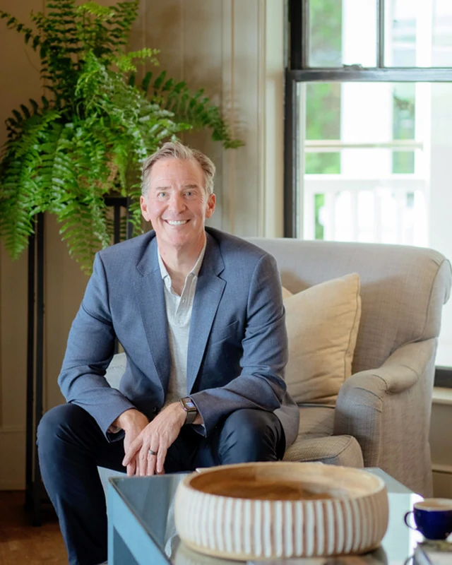 Mark Zides seated in an armchair in a bright room, in a navy blazer.